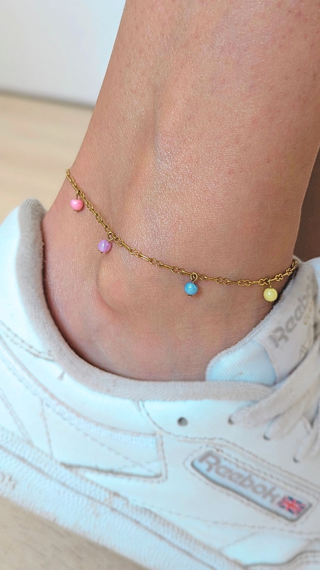 chaine de cheville dorée avec 4 perles de couleurs rose jaune bleu et violet porté à la cheville avec des baskets blanches
