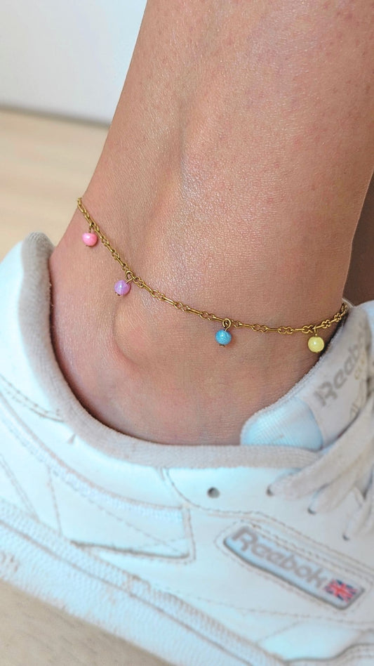chaine de cheville dorée avec 4 perles de couleurs rose jaune bleu et violet porté à la cheville avec des baskets blanches